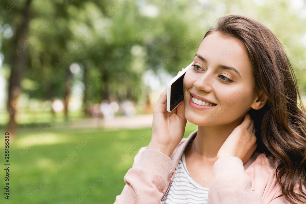 attractive girl talking on smartphone and smiling in park