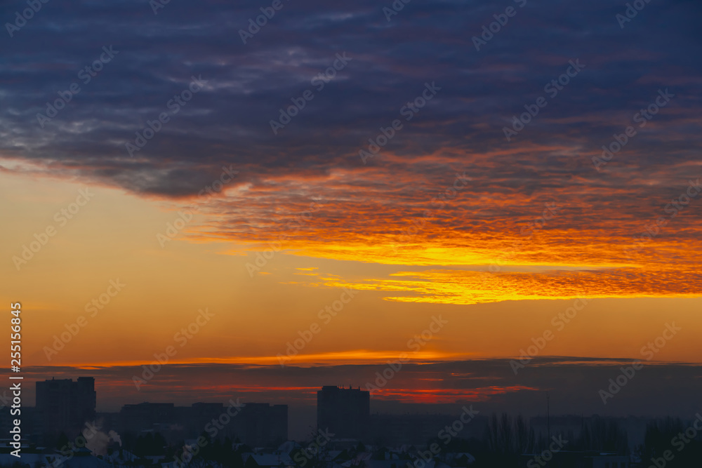 Cityscape with wonderful varicolored fiery dawn. Amazing dramatic multicolored cloudy sky. Dark silhouettes of city building roofs. Atmospheric background of sunrise in overcast weather. Copy space. Cityscape with wonderful varicolored fiery dawn. Amazing dramatic multicolored cloudy sky. Dark silhouettes of city building roofs. Atmospheric background of sunrise in overcast weather. Copy space.