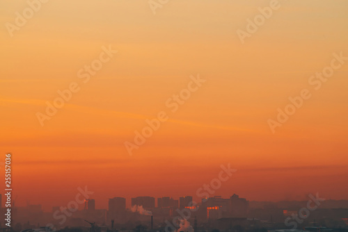 Urban high-rise buildings behind private houses on sunset. Silhouettes of big city buildings. Warm backlight of dawn. Private sector near apartment houses in sunlight. Minimalist cityscape at sunrise.