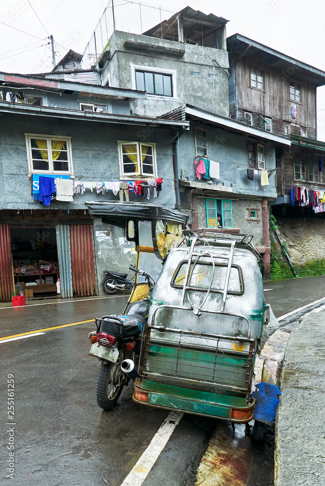 A Motorcycle with sidecar parking along a curved road in Banaue Town, Ifugao Province, Philippines, with typical simple buildings in the background.