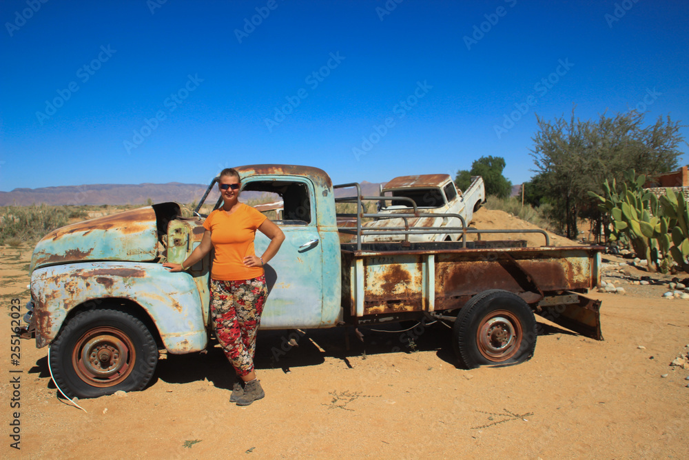 Obraz premium Abandoned old rusty cars in the desert of Namibia and a plump white tourist girl near the Namib-Naukluft National Park. Africa