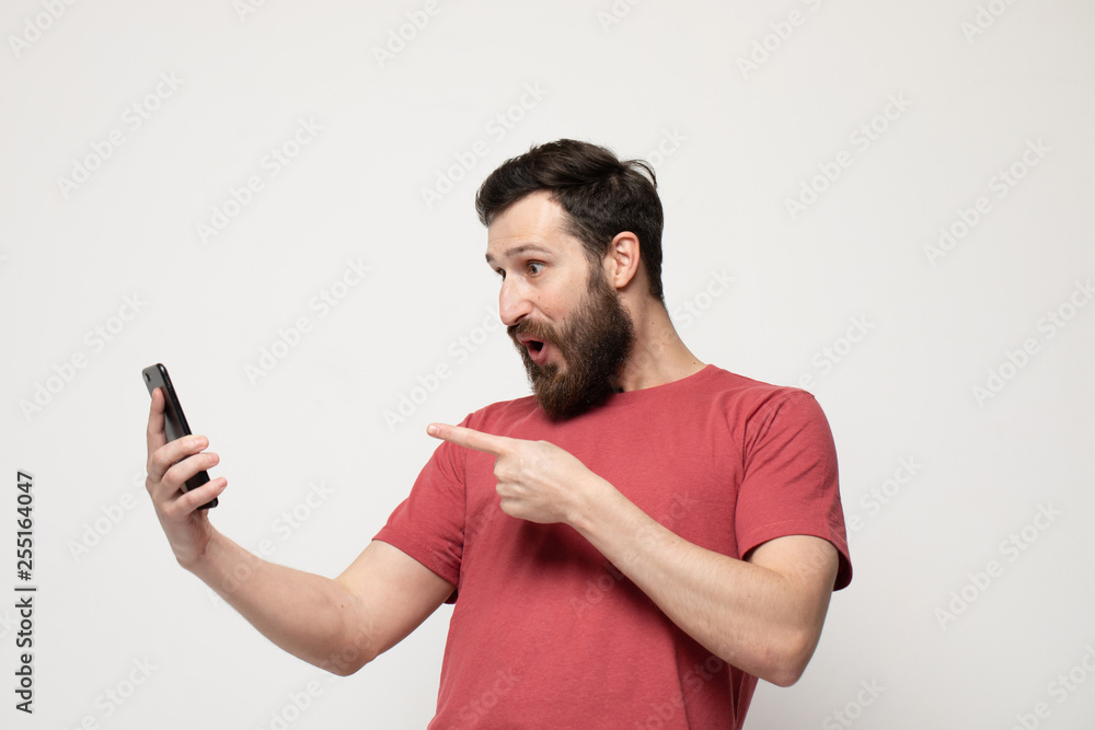 Portrait of a cheerful young man wearing casual clothes standing isolated over grey background, using mobile phone Portrait of a cheerful young man wearing casual clothes standing isolated over grey background, using mobile phone
