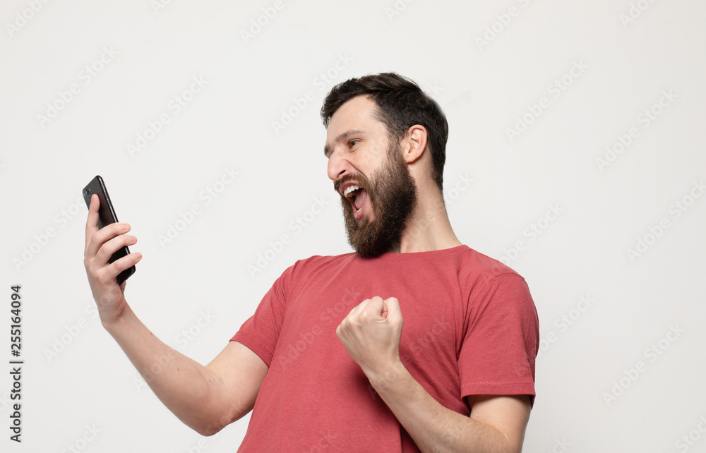 Portrait of a cheerful young man wearing casual clothes standing isolated over grey background, using mobile phone Portrait of a cheerful young man wearing casual clothes standing isolated over grey background, using mobile phone