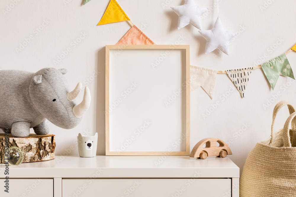 The modern scandinavian newborn baby room with mock up photo frame, wooden car, plush rhino and clouds. Hanging cotton flags and white stars. Minimalistic and cozy interior with white walls.Real photo - obrazy, fototapety, plakaty 