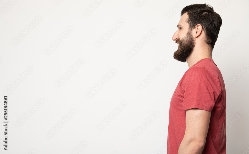 Side view portrait of confident bearded man with beautiful hairstyle in red t-shirt looking on copy space Side view portrait of confident bearded man with beautiful hairstyle in red t-shirt looking on copy space