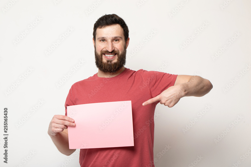 Young bearded man with blank pink banner. Smiling man holding advertising sheet, copy space, isolated Young bearded man with blank pink banner. Smiling man holding advertising sheet, copy space, isolated