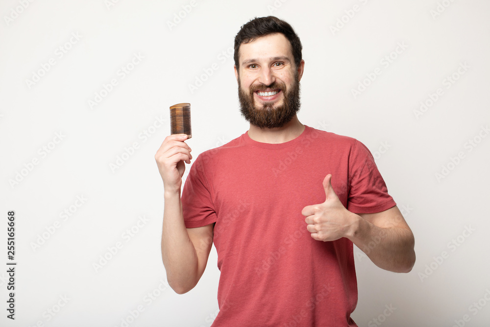 Attractive smiling Bearded man holding a comb for beard standing above grey background Attractive smiling Bearded man holding a comb for beard standing above grey background