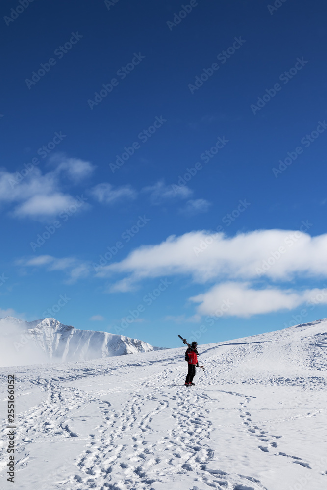 Skier with skis on his shoulder and snowy mountain