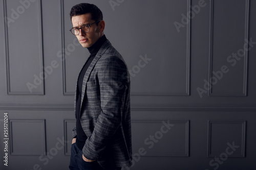 фотографія Attractive, strong, muscular young man dressed elegantly suit posing in studio, standing near wall, shadows background