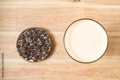 A glass cup of pearl milk tea (also called bubble tea) and a plate of tapioca ball on wooden background. Pearl milk tea is the most representative drink in Taiwan. Taiwan food . With copy space.