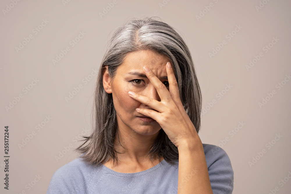 Woman of Mongolian Appearance with a Sad Look on a Gray Background. Woman of Mongolian Appearance with a Sad Look on a Gray Background.