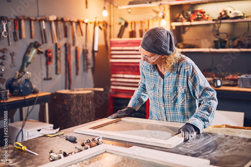 Woman carpenter sanding old window in a retro workshop.