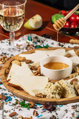 Cheese plate and chef hand wich pours honey: Sulguni, Guda, cheddar, gouda, camembert, and other served with white wine, honey and nuts on wooden board on light background. Tasty appetizers.