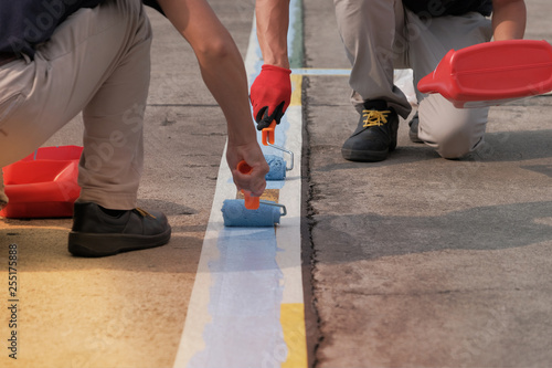 Specialist painters working together for painting blue lines striping on concrete floor of parking lots in car park. Profestional painter man at work with a roller, Blank for text with copy space. photo