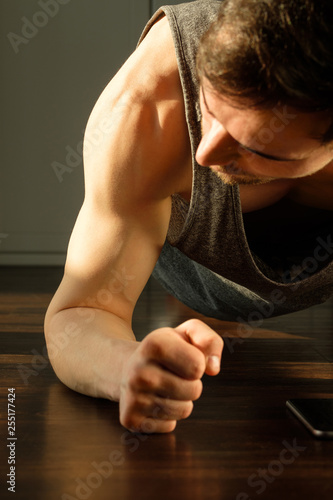 A handsome man doing plank exercises against the window of a house