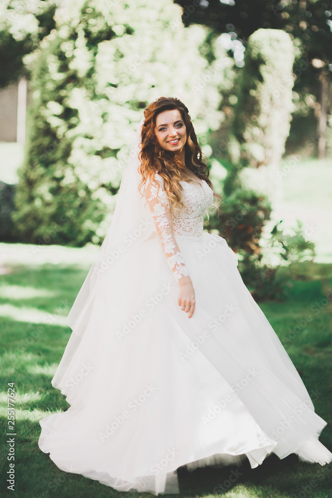 Beautiful bride in elegant white dress holding bouquet posing in park