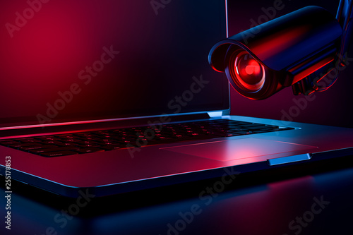 Computer observed by hostile looking camera as a metaphor of stalking or malicious software observing and tracking user. Copy space on laptop screen included. 3D rendering photo