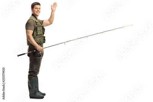 Young male fisherman holding a fishing rod and waving at the camera