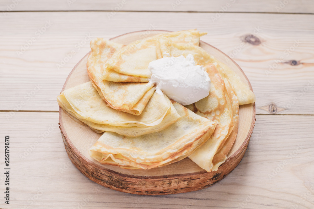 Russian thin pancakes on a wooden stand made of natural wood with sour cream . Maslenitsa is a Maslenitsa food festival. Russian thin pancakes on a wooden stand made of natural wood with sour cream . Maslenitsa is a Maslenitsa food festival.