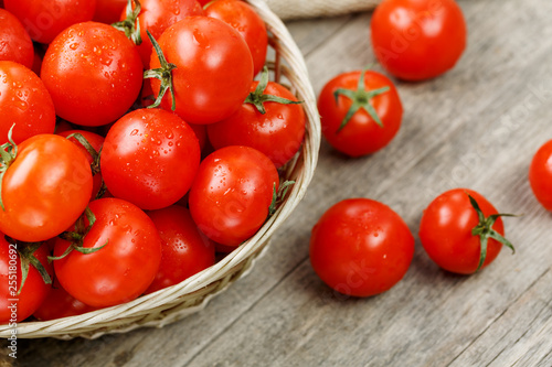 Fresh red tomatoes in a wicker basket on an old wooden table. Ripe and juicy cherry tomatoes with drops of moisture, gray wooden table, around a cloth of burlap. In a rustic style.