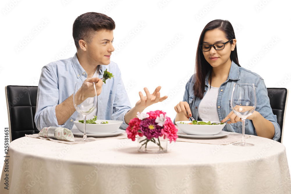 Young male and female eating a salad at a restaurant table and talking Young male and female eating a salad at a restaurant table and talking