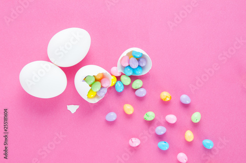 colourful easter eggs spilling out of a white egg shell on a pink background