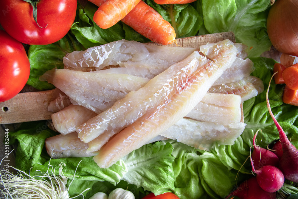 Raw hake fish fillets pieces with organic fresh vegetables in the background Raw hake fish fillets pieces with organic fresh vegetables in the background