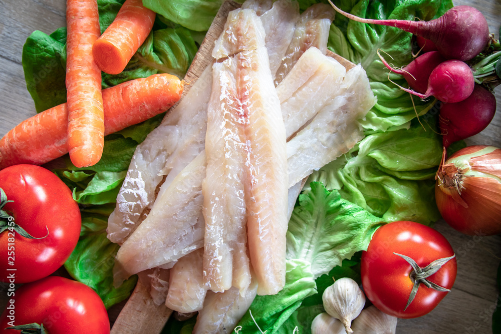 Raw hake fish fillets pieces with organic fresh vegetables in the background Raw hake fish fillets pieces with organic fresh vegetables in the background