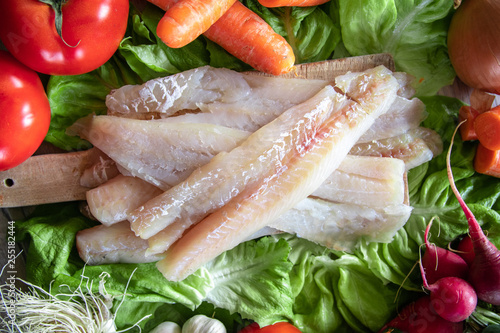 Raw hake fish fillets pieces with organic fresh vegetables in the background