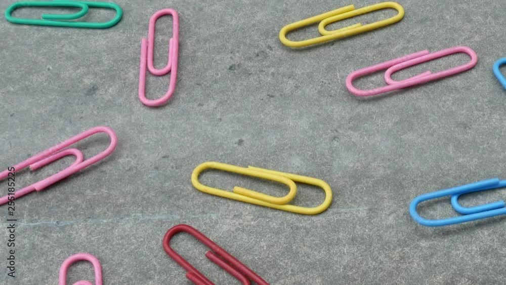 Spread multi color paper clips isolated on grey background; moving from left to right. Useful as background. Spread multi color paper clips isolated on grey background; moving from left to right. Useful as background.