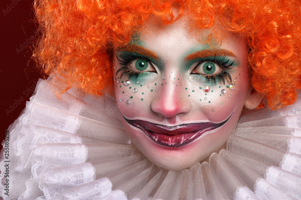 Cute red-haired clown.Girl in bright clown makeup. Close up. Stock Photo
