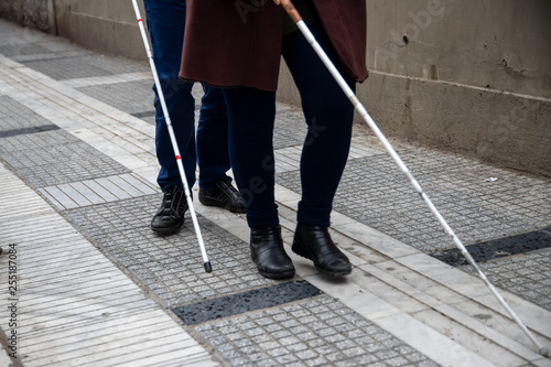 blind man and woman walking on the street using a white walking stick