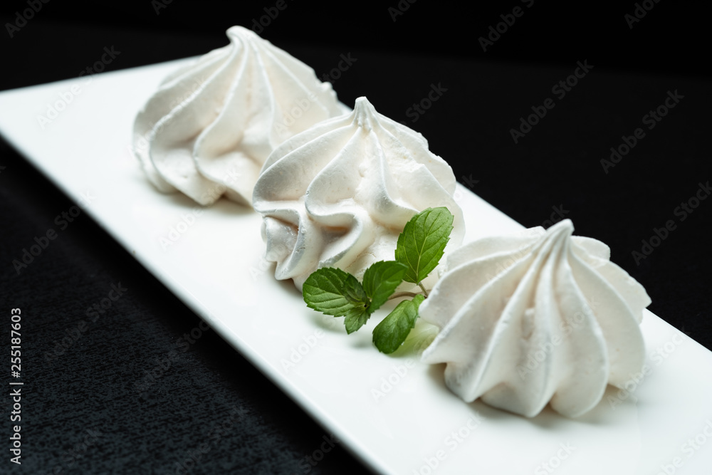 meringue meringue protein dessert in a white plate on a black background decorated with mint