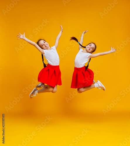 funny children girls twins jumping on colored yellow background.
