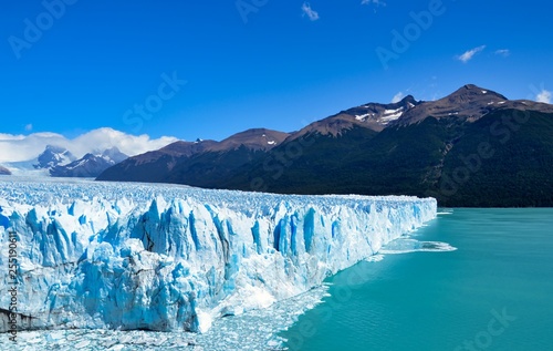 View of a branch of the Perito Moreno progressing into the water of the lake, with mountains in the background.