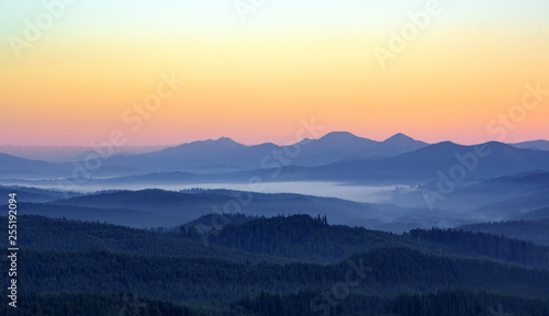 Foggy morning in the mountains with silhouettes of hills. Serenity sunrise with soft sunlight and layers of haze. Mountain landscape with mist in woodland in pastel colors