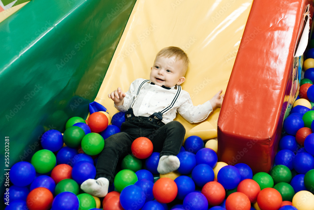Cute kid playing in the children's center, moves down the hill in the balls. Funny childhood