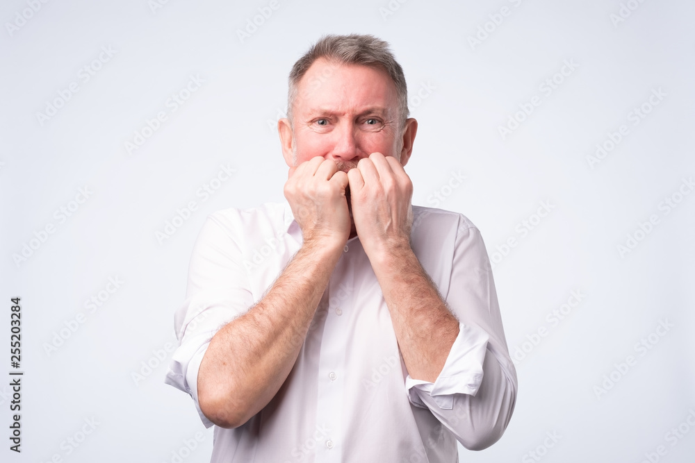 Senior man in white shirt biting nails in fear Senior man in white shirt biting nails in fear
