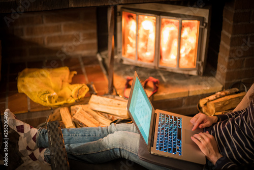 Cozy home. Pretty young woman working on laptop computer near the fireplace.