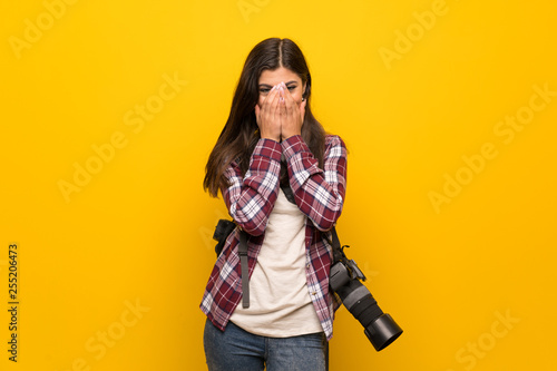 Photographer teenager girl over yellow wall smiling a lot