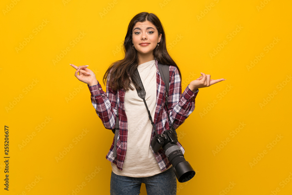 Photographer teenager girl over yellow wall pointing to the laterals having doubts Photographer teenager girl over yellow wall pointing to the laterals having doubts