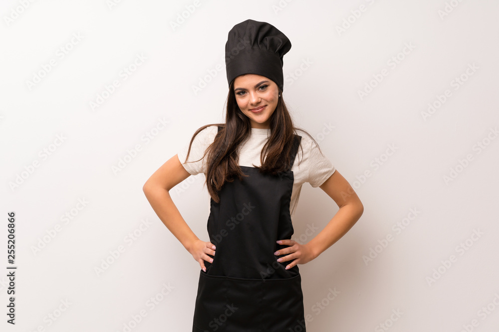 Teenager chef over white wall posing with arms at hip and smiling Teenager chef over white wall posing with arms at hip and smiling