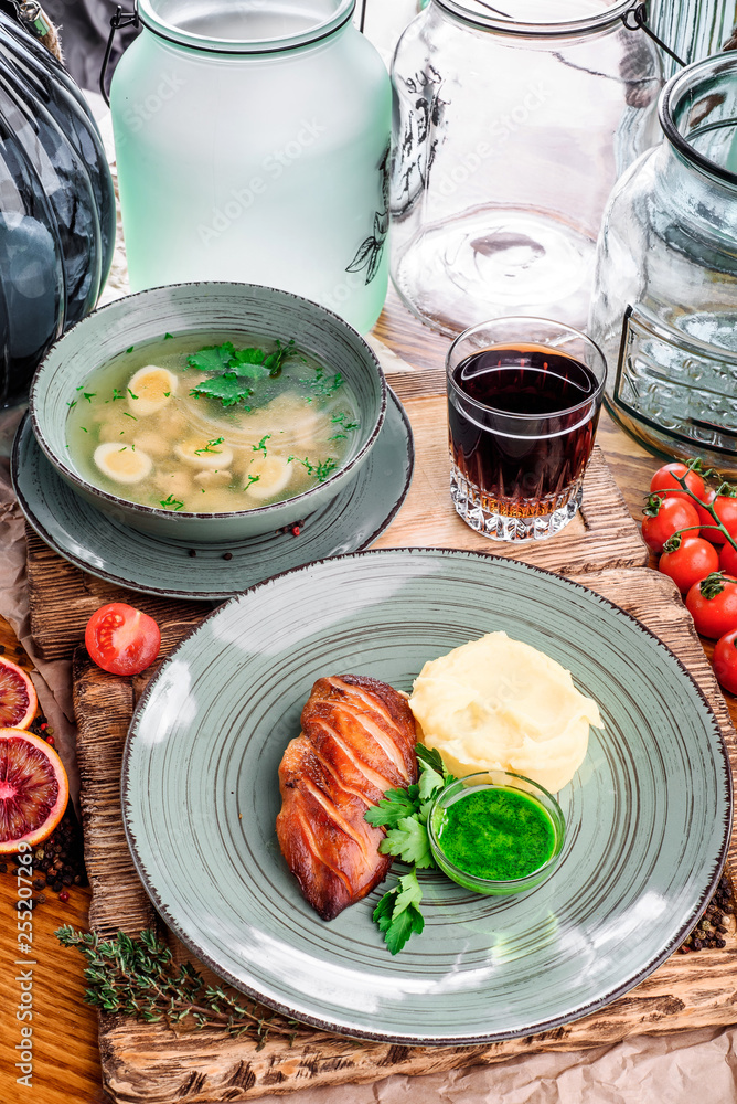 Grape juice and lunch from chicken breast and mashed potatoes, chicken broth with quail eggs in gray plates on wooden boards in rustic composition. national Ukrainian and Russian dishes Grape juice and lunch from chicken breast and mashed potatoes, chicken broth with quail eggs in gray plates on wooden boards in rustic composition. national Ukrainian and Russian dishes