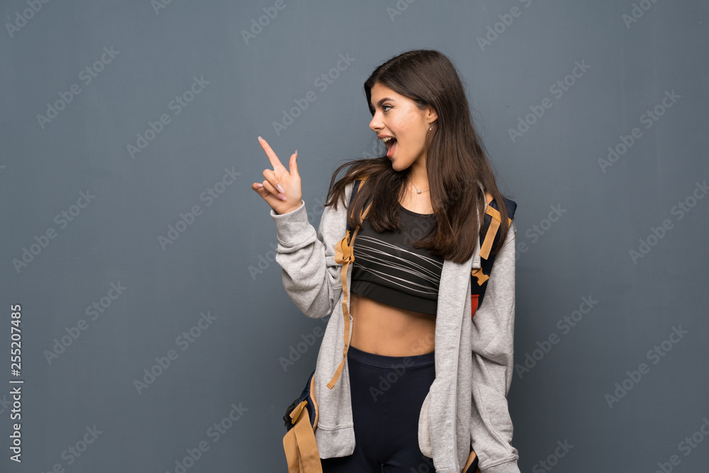 Teenager traveler girl over wall surprised and pointing finger to the side Teenager traveler girl over wall surprised and pointing finger to the side
