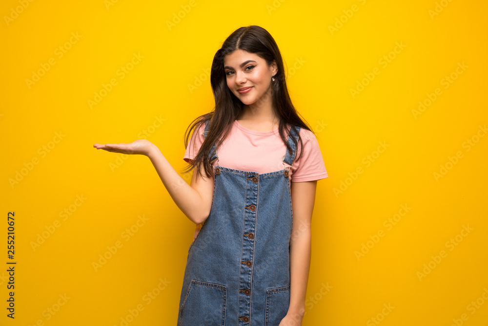 Teenager girl over yellow wall holding copyspace imaginary on the palm to insert an ad Teenager girl over yellow wall holding copyspace imaginary on the palm to insert an ad