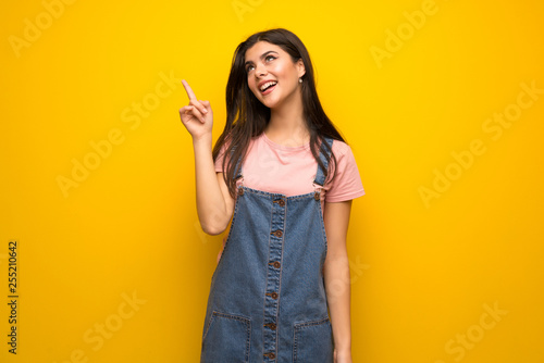 Teenager girl over yellow wall intending to realizes the solution while lifting a finger up
