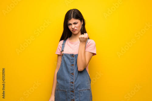 Teenager girl over yellow wall with angry gesture
