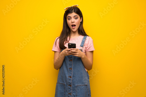 Teenager girl over yellow wall surprised and sending a message