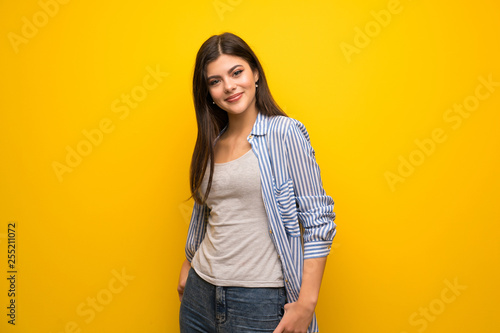 Teenager girl over yellow wall laughing looking to the front
