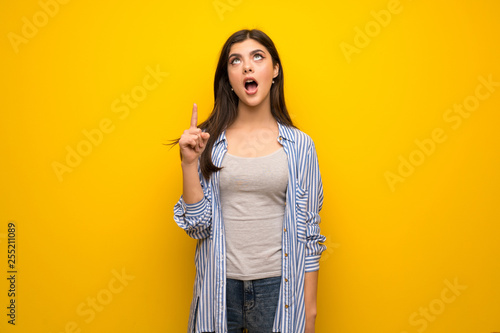 Teenager girl over yellow wall thinking an idea pointing the finger up © luismolinero